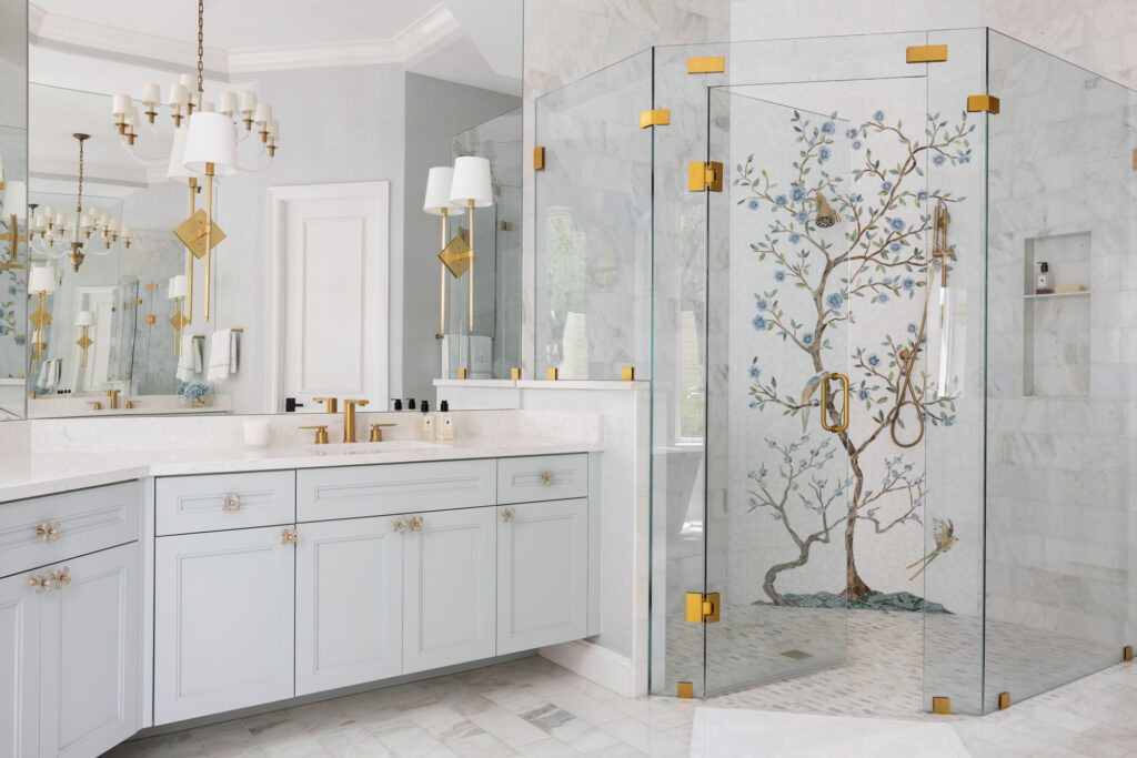 Luxury primary bathroom featuring a custom glass walk-in shower with a hand-painted Chinoiserie tree mural, gold hardware, and a light blue vanity with floral knobs