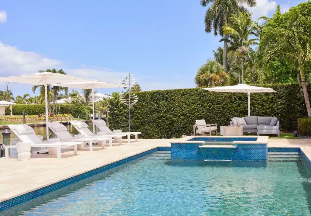 Modern resort-style pool patio featuring custom outdoor furniture, stone pavers, and lush South Florida landscaping