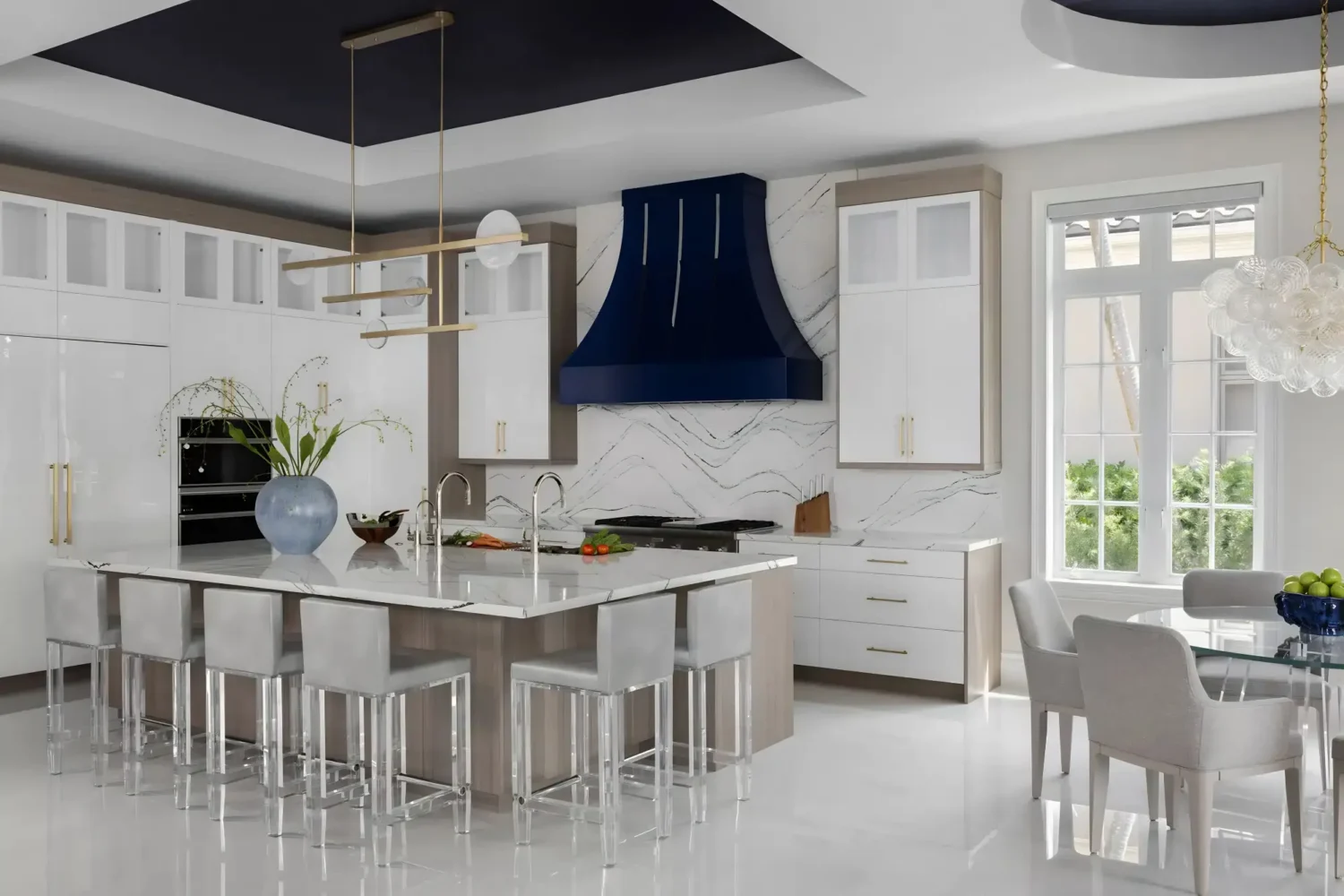Luxury kitchen design with two-tone cabinetry, a large marble waterfall island with seating, a custom navy blue range hood, brass hardware, and modern pendant lighting