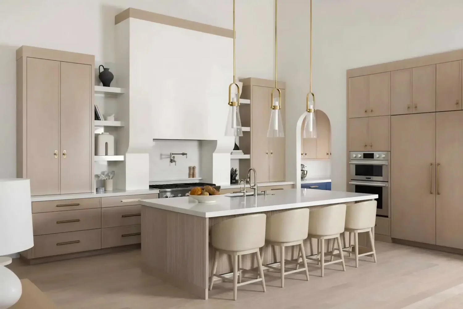 Light, neutral kitchen with custom beige cabinetry, large white island with seating, brass pendant lights, and integrated built-in appliances in a modern luxury interior.